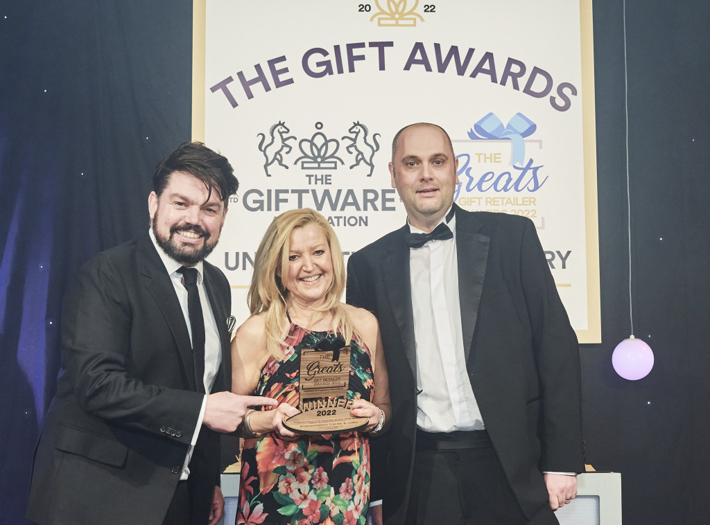 Above: Andrea Pinder, owner of Presentation Cards & Gifts in Barrowford, was presented with a Greats trophy in 2922 by David Cree, sales manager of Joe Davies, category sponsor. On the left is compere and comedian Charlie Baker.